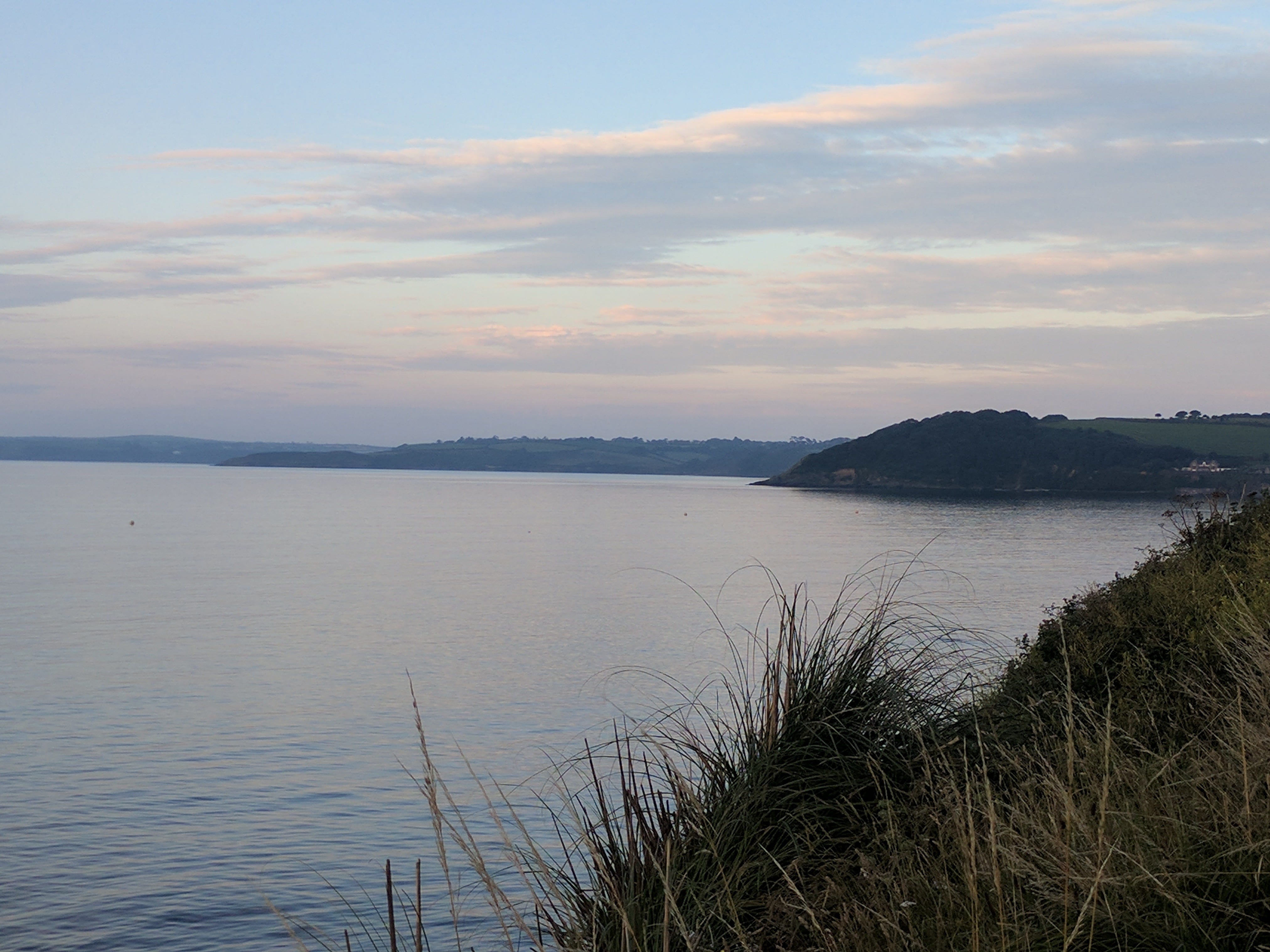 A headland is in the distance. In the foreground there is sea. It's a calm sky.