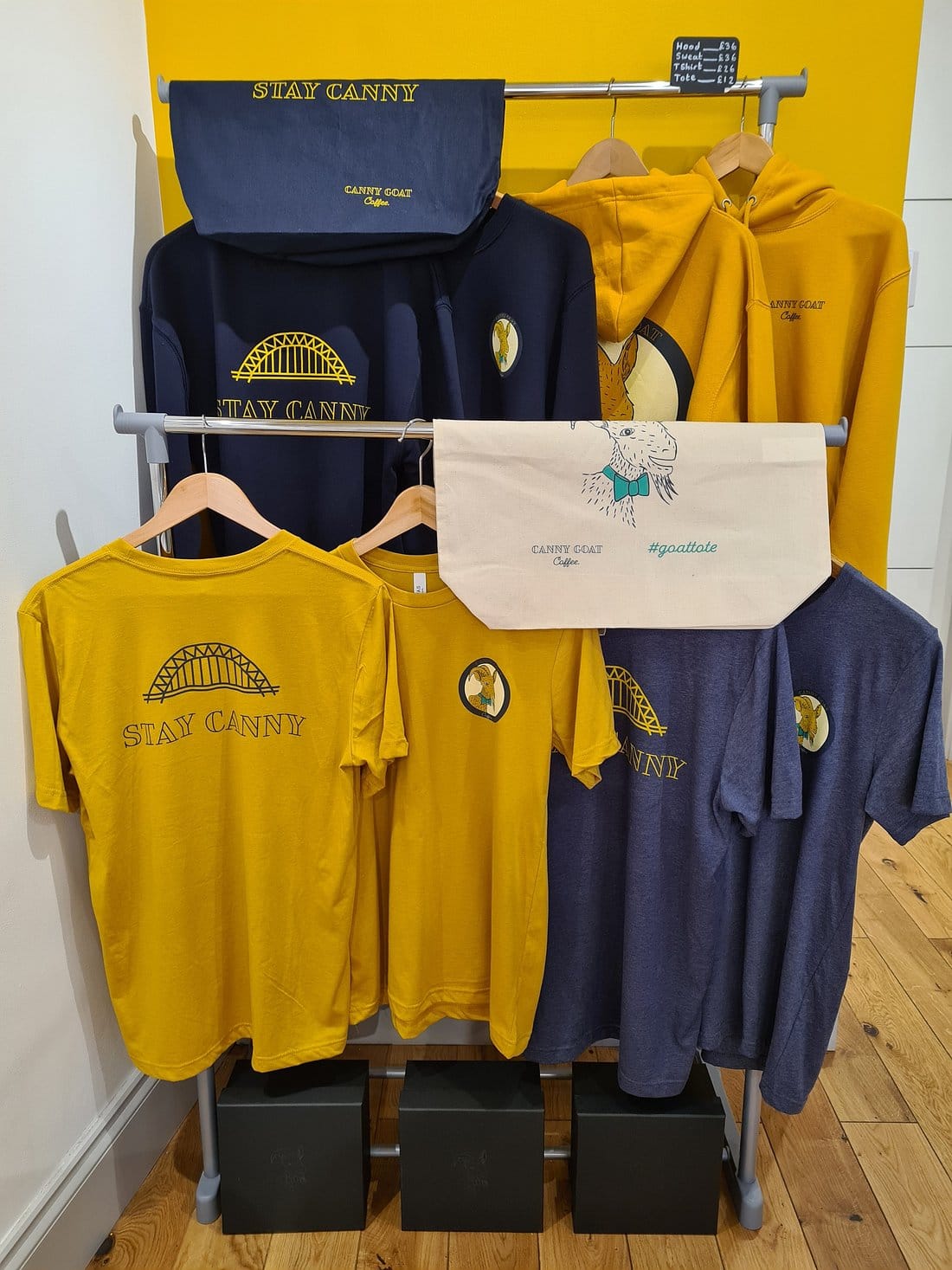 An array of yellow and blue t-shirts with the Tyne Bridge on, the words "Stay Canny", and the Canny Goat logo (a goat!)